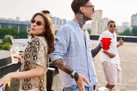 jolly multiracial friends with sunglasses drinking cocktails at rooftop party and dancing to DJ set