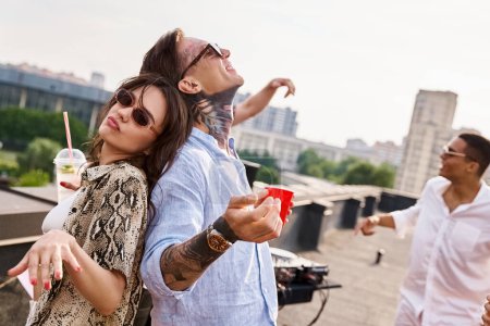 joyous diverse friends with sunglasses drinking cocktails at rooftop party and chilling to DJ set