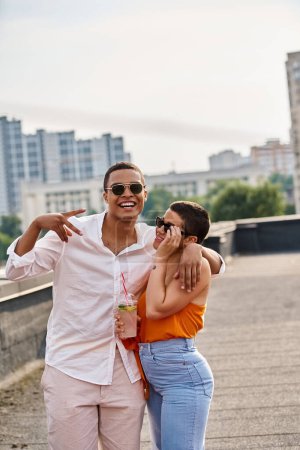 joyous interracial man and woman in casual attires chilling at rooftop party with cocktails
