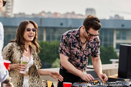 fröhliche Frau mit stylischer Sonnenbrille und Cocktail in der Hand posiert neben DJ auf Dachparty