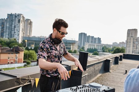 Photo for Handsome young male DJ with stylish sunglasses in urban casual attire playing music at rooftop party - Royalty Free Image