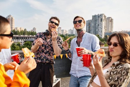 Téléchargez les photos : Joyeux amis attrayants dans des vêtements urbains élégants manger de la pizza et profiter des boissons à la fête - en image libre de droit