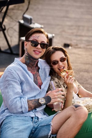 Téléchargez les photos : Amis joyeux avec des lunettes de soleil à la mode profitant de pizza et cocktails à la fête et souriant à la caméra - en image libre de droit