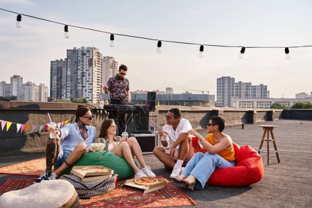Téléchargez les photos : Amis interracial joyeux en tenue décontractée profiter de cocktails à la fête sur le toit avec DJ sur toile de fond - en image libre de droit