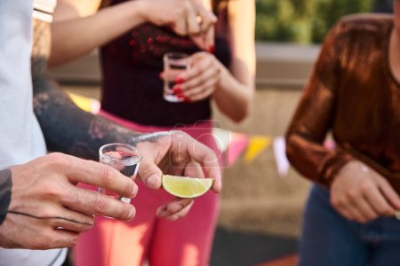 Téléchargez les photos : Vue recadrée de jeunes amis en tenue décontractée se préparant à boire de la tequila au citron vert et au sel - en image libre de droit