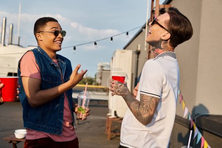 Zwei multiethnische Freunde in lässiger Kleidung mit Sonnenbrille amüsieren sich gemeinsam auf einer Dachparty