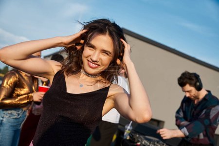 focus on merry appealing woman in urban attire partying next to her jolly blurred friends on rooftop