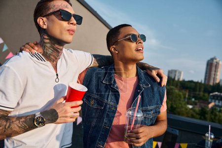 gutaussehende multikulturelle Männer in lebendiger Kleidung genießen Drinks und schauen von der Dachterrassenparty weg