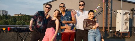 Foto de Felices jóvenes amigos multirraciales en trajes urbanos de moda sonriendo a la cámara en la fiesta en la azotea, pancarta - Imagen libre de derechos
