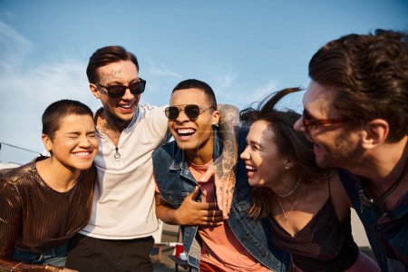 Téléchargez les photos : Attrayant divers amis joyeux avec des lunettes de soleil ayant beaucoup de temps ensemble à la fête sur le toit - en image libre de droit