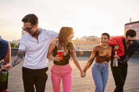 Téléchargez les photos : Amis multiculturels joyeux dans des tenues vibrantes tenant des boissons alcoolisées et s'amusant à la fête - en image libre de droit