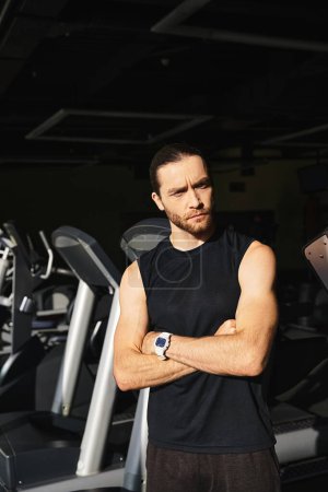 Ein athletischer Mann in Aktivkleidung steht selbstbewusst vor einer Reihe von Laufbändern in einem Fitnessstudio, bereit, sein Workout zu beginnen.