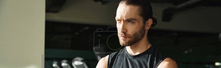 Ein muskulöser Mann in schwarzem Tanktop steht selbstbewusst in einem Fitnessstudio.