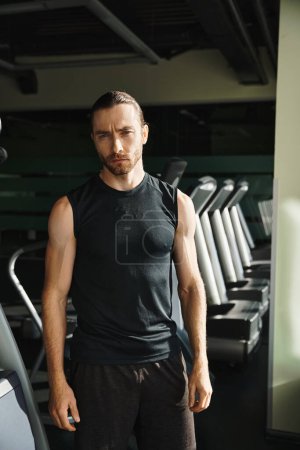 Ein athletischer Mann in aktiver Kleidung steht selbstbewusst vor einer Reihe von Laufbändern, bereit für eine herausfordernde Trainingseinheit.