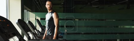 Ein athletischer Mann in aktiver Kleidung steht vor einer Reihe von Laufbändern, bereit für eine Trainingseinheit.