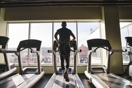 A fit man in activewear runs on a treadmill in a gym, putting in effort and energy into his workout routine.