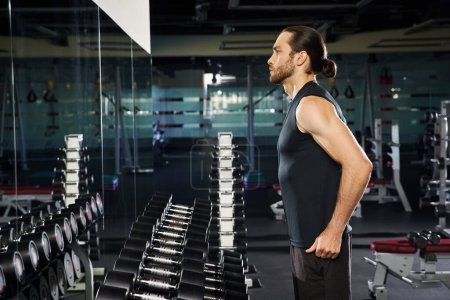 An athletic man in active wear confidently standing in front of a rack of dumbbells, preparing for a workout session.