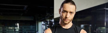 Photo for A man in active wear stands in front of a mirror at the gym, examining his form and muscles after a workout. - Royalty Free Image