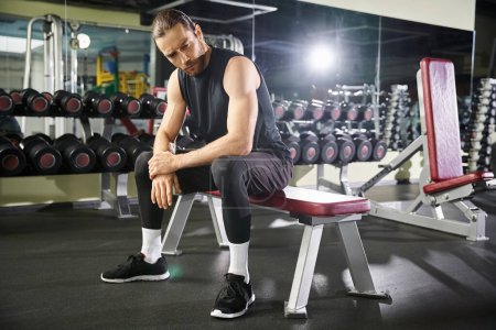 Téléchargez les photos : Un homme sportif en tenue active prenant une pause, assis sur un banc dans une salle de gym. - en image libre de droit