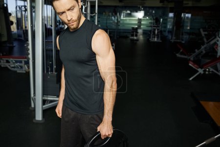 An athletic man in active wear holding a black plate in a gym.