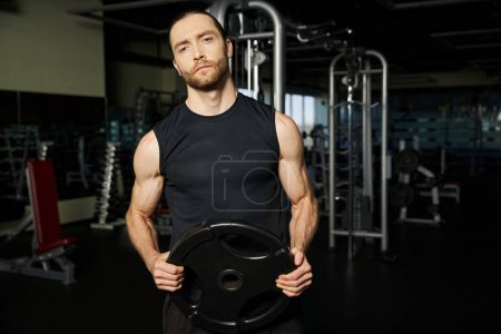 Ein athletischer Mann in aktiver Kleidung hält beim Training im Fitnessstudio eine schwarze Platte in der Hand.
