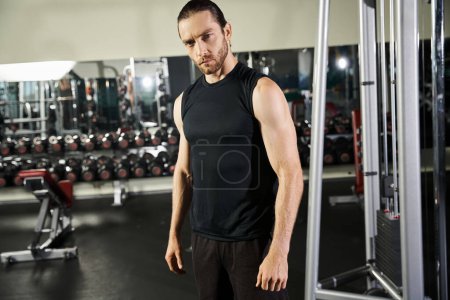 Ein athletischer Mann in aktiver Kleidung steht selbstbewusst vor einem Fitnessgerät, bereit zum Training und Kraftaufbau.