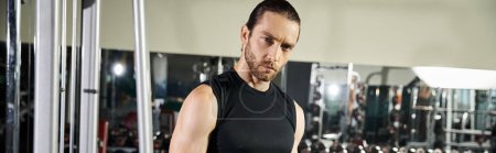 Un hombre en forma en una camiseta negra está realizando ejercicios en un gimnasio bien equipado, centrándose en el entrenamiento de fuerza y resistencia..