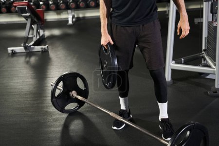Homme athlétique dans la salle de gym près de Barbell, mettant en valeur la force et la détermination lors d'une séance d'entraînement intense.