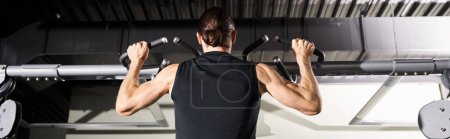 A determined man in a black shirt performs a pull-up, showcasing strength and perseverance in a gym setting.