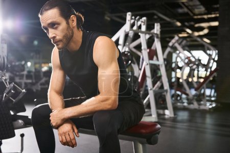 Un hombre atlético en ropa activa sentado en un banco de gimnasia, tomando un momento para descansar y reflexionar sobre su sesión de entrenamiento.