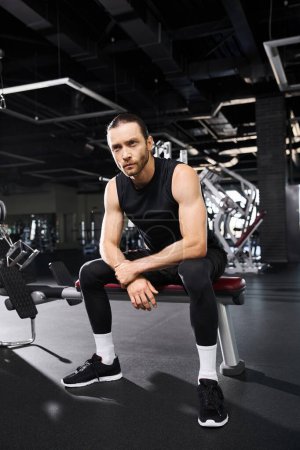Ein athletischer Mann in aktiver Kleidung sitzt auf einer Gymnastikbank und ruht sich während seiner Trainingseinheit aus.