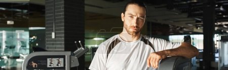 Ein fitter Mann in Sportkleidung steht neben einem Gerät im Fitnessstudio.