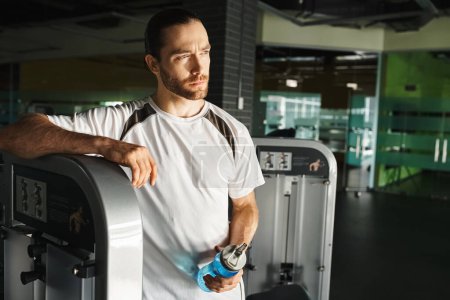 Téléchargez les photos : Un homme athlétique en tenue active debout avec confiance à côté d'une machine de gymnastique. - en image libre de droit