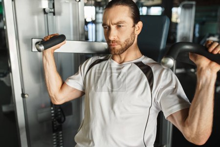Ein athletischer Mann in aktiver Kleidung, der einen Griff an einem Trainingsgerät hält, während er im Fitnessstudio trainiert.