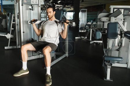 Un hombre atlético en ropa activa sentado en un banco de gimnasio, sosteniendo asas en la máquina de ejercicios