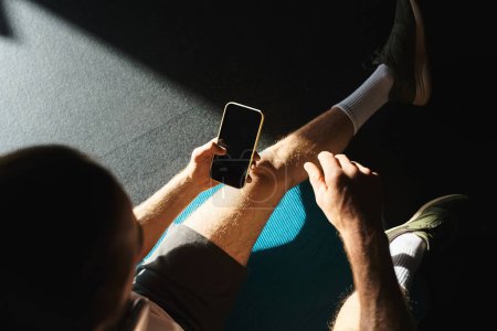 Foto de Un hombre en ropa activa sostiene un teléfono inteligente en sus manos, centrado en la pantalla. - Imagen libre de derechos