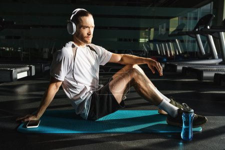 Ein athletischer Mann sitzt auf einer blauen Matte und trägt Kopfhörer, eingetaucht in einen Moment der Entspannung und Musik..