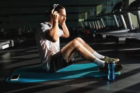 Un hombre en ropa activa se sienta en una alfombra azul, dedicado a una música en el gimnasio
