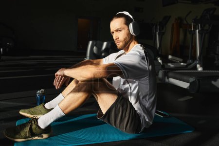 Un hombre atlético en ropa activa se sienta en una alfombra, inmerso en la música a través de auriculares.