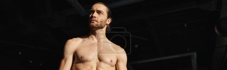 Photo for A muscular man in a dark space, shirtless and standing confidently, banner - Royalty Free Image