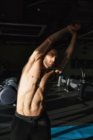 Un hombre musculoso sin camisa sosteniendo sus brazos en triunfo en el gimnasio.