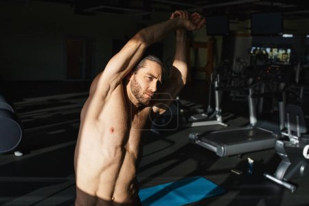 A muscular man without a shirt is diligently working out in a gym environment.
