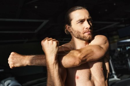 Hemdloser Mann mit muskulösem Körperbau, der in einem Fitnessstudio mit Selbstvertrauen und Entschlossenheit den Bizeps beugt.
