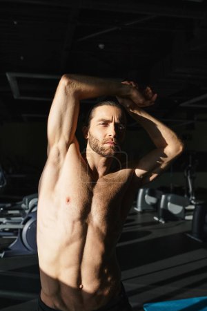 A muscular man without a shirt is warming up before work out in a gym.