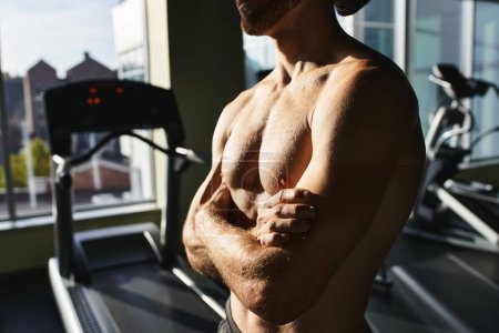 Muscular man, shirtless, next to treadmill in gym.