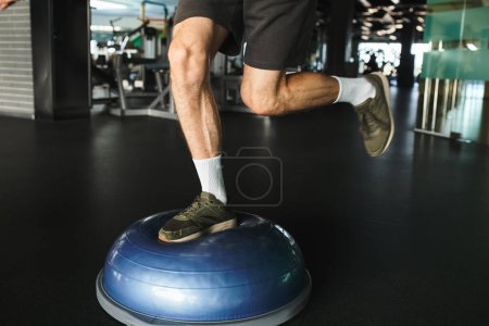 Ausgeschnittene Ansicht eines Mannes, der in der Turnhalle auf einem blauen Turnball trainiert.