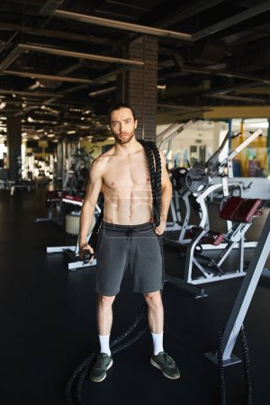 Ein muskulöser Mann ohne Hemd, der in einem Fitnessstudio steht und sein Engagement für Fitness und Krafttraining demonstriert.