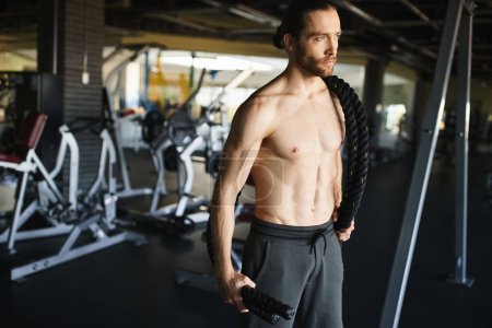 Ein muskulöser Mann steht selbstbewusst in einem Fitnessstudio, konzentriert auf sein Workout-Programm und demonstriert seine Hingabe zum Kraftaufbau.