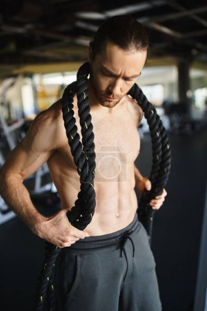Ein muskulöser Mann ohne Hemd mit einem Seil um Hals und Körper, während er in einem Fitnessstudio trainiert.