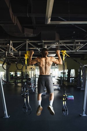 Muskulöser Mann ohne Hemd macht Klimmzüge an der Bar in einem Fitnessstudio.